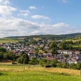 Panoramablick auf Eibach bei Dillenburg Eine Panoramafotografie von Eibach bei Dillenburg, umgeben von grünen Feldern und Wäldern unter einem bewölkten Himmel. Im Hintergrund sind Hügel und Windkraftanlagen sichtbar.
