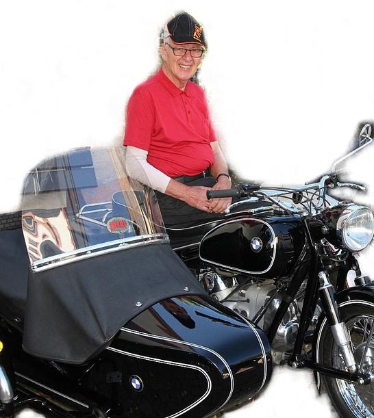 &Auml;lterer Mann in rotem Shirt sitzt auf einer schwarzen BMW mit Beiwagen und l&auml;chelt in die Kamera.