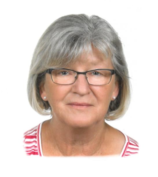 Portr&auml;t einer &auml;lteren Frau mit grauen Haaren und Brille, l&auml;chelnd vor neutralem Hintergrund. Sie tr&auml;gt ein gestreiftes Shirt.