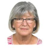 Portr&auml;t einer &auml;lteren Frau mit grauen Haaren und Brille, l&auml;chelnd vor neutralem Hintergrund. Sie tr&auml;gt ein gestreiftes Shirt.