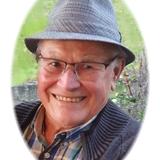 L&auml;chelnder &auml;lterer Mann mit Brille und Hut, Portr&auml;t vor gr&uuml;nem Hintergrund.