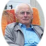 &Auml;lterer Mann mit Brille sitzt entspannt auf einem orangefarbenen Stuhl mit floralen Motiven im Freien.