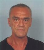 Portr&auml;t eines Mannes mit kurzem grauem Haar, goldener Kette und schwarzem Hemd, vor einem hellblauen Hintergrund.