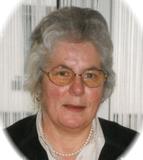 Portr&auml;t einer Frau mit grauen Haaren, Brille und Perlenkette vor einem hellen Hintergrund.