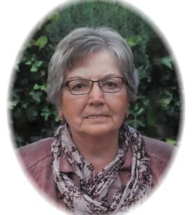 Portr&auml;t einer &auml;lteren Frau mit Brille und grauen Haaren, umgeben von gr&uuml;ner Vegetation. Sie tr&auml;gt einen lila Schal.