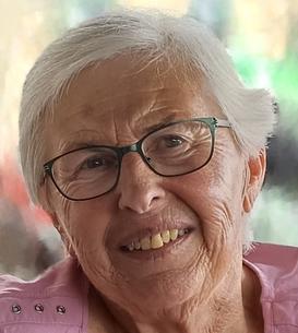 L&auml;chelnde &auml;ltere Frau mit kurzen grauen Haaren und Brille, getragenes pinkes Oberteil, unscharfer bunter Hintergrund.