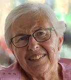 L&auml;chelnde &auml;ltere Frau mit kurzen grauen Haaren und Brille, getragenes pinkes Oberteil, unscharfer bunter Hintergrund.