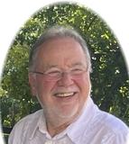 L&auml;chelnder Mann mit Brille und wei&szlig;em Hemd, umgeben von gr&uuml;nem Hintergrund. Ovaler Zuschnitt des Fotos.