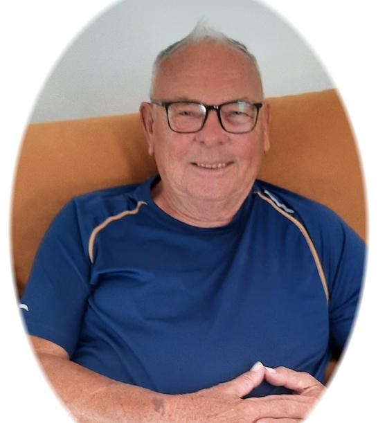 Portr&auml;t eines &auml;lteren Mannes mit Brille, der in einem blauen Shirt auf einem Sofa sitzt und l&auml;chelt.