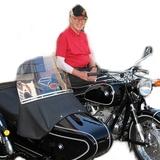 Älterer Mann in rotem Shirt sitzt auf einer schwarzen BMW mit Beiwagen und lächelt in die Kamera.