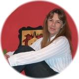 Frau mit langem Haar in gestreiftem Hemd sitzt mit angezogenen Beinen vor roter Wand und einem hölzernen Kunstwerk.