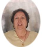 Porträt einer Frau mittleren Alters mit kurzen, lockigen Haaren und goldener Halskette, lächelnd vor neutralem Hintergrund.