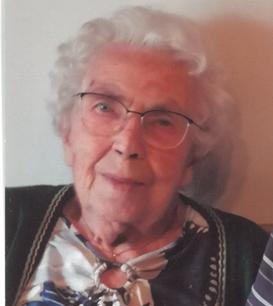 Ältere Frau mit Brille und lockigem, grauem Haar, in einem gemusterten Oberteil, lächelt leicht in die Kamera.