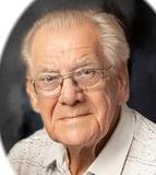 Portrait eines älteren Mannes mit Brille, der einen hellen Hemdkragen trägt, vor einem dunklen Hintergrund.