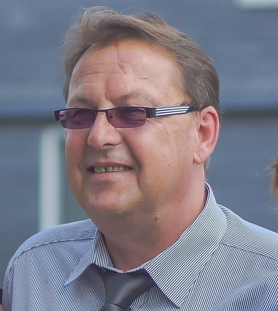 Mann mit Brille und gestreiftem Hemd lächelt vor einem neutralen Hintergrund.