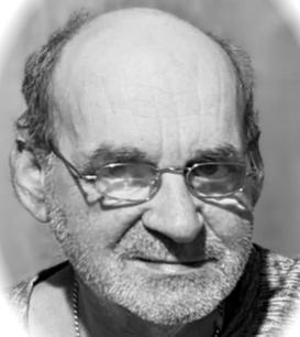 Porträt eines älteren Mannes mit Glatze und Brille, der ernst in die Kamera schaut, vor einem unscharfen Hintergrund.