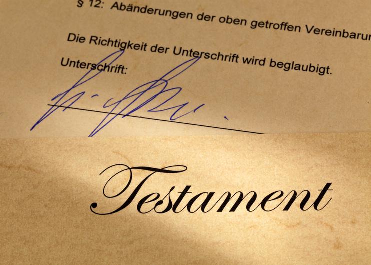Nahaufnahme eines Testaments auf beige-farbenem Papier mit einer blauen Unterschrift. Der Text bestätigt die Beglaubigung der Unterschrift.